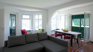 Una sala de estar moderna con un sofá modular gris, una mesa de comedor con sillas y un ventanal con persianas.