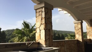 Cozinha externa com parede de pedra e vista para uma paisagem exuberante.