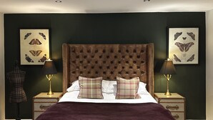 Une chambre à coucher avec une tête de lit capitonnée, deux tables de chevet avec des lampes, un plaid et des œuvres d’art sur le thème des papillons accrochées aux murs.