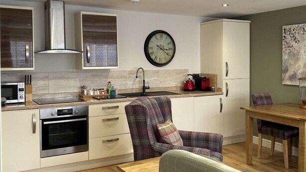 Une cuisine moderne dotée d’appareils électroménagers intégrés, un coin repas avec une table et des chaises en bois, et une horloge au mur.