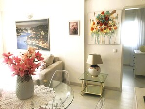 A living room with a sofa, a glass coffee table, a vase with flowers, a lamp, and wall art. - Ocean front apartment with sea view situated in prime area of pear frame (Armação de Pêra)