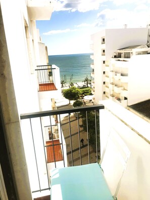 A balcony with a view of the sea, a building with a balcony, and a street with a tree. - Ocean front apartment with sea view situated in prime area of pear frame (Armação de Pêra)