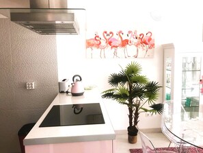 A kitchen with a modern stove, a small island, a potted plant, and a painting of flamingos on the wall. - Ocean front apartment with sea view situated in prime area of pear frame (Armação de Pêra)
