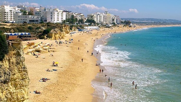 Una playa con gente, una orilla arenosa y edificios al fondo.