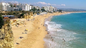 A beach with buildings in the background, sandy shore, and clear blue water. - Ocean front apartment with sea view situated in prime area of pear frame (Armação de Pêra)