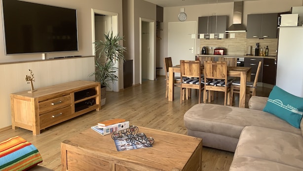 A modern living room with a flat-screen TV, wooden furniture, a coffee table with magazines, and a sofa with a teal pillow. - Comfortable holiday apartment within walking distance of the beach, Fehmarn Golf Park and surfing area  (Fehmarn)