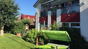 A residential building with a red facade, balconies with potted plants, and a green awning in the foreground. - Comfortable holiday apartment within walking distance of the beach, Fehmarn Golf Park and surfing area  (Fehmarn)
