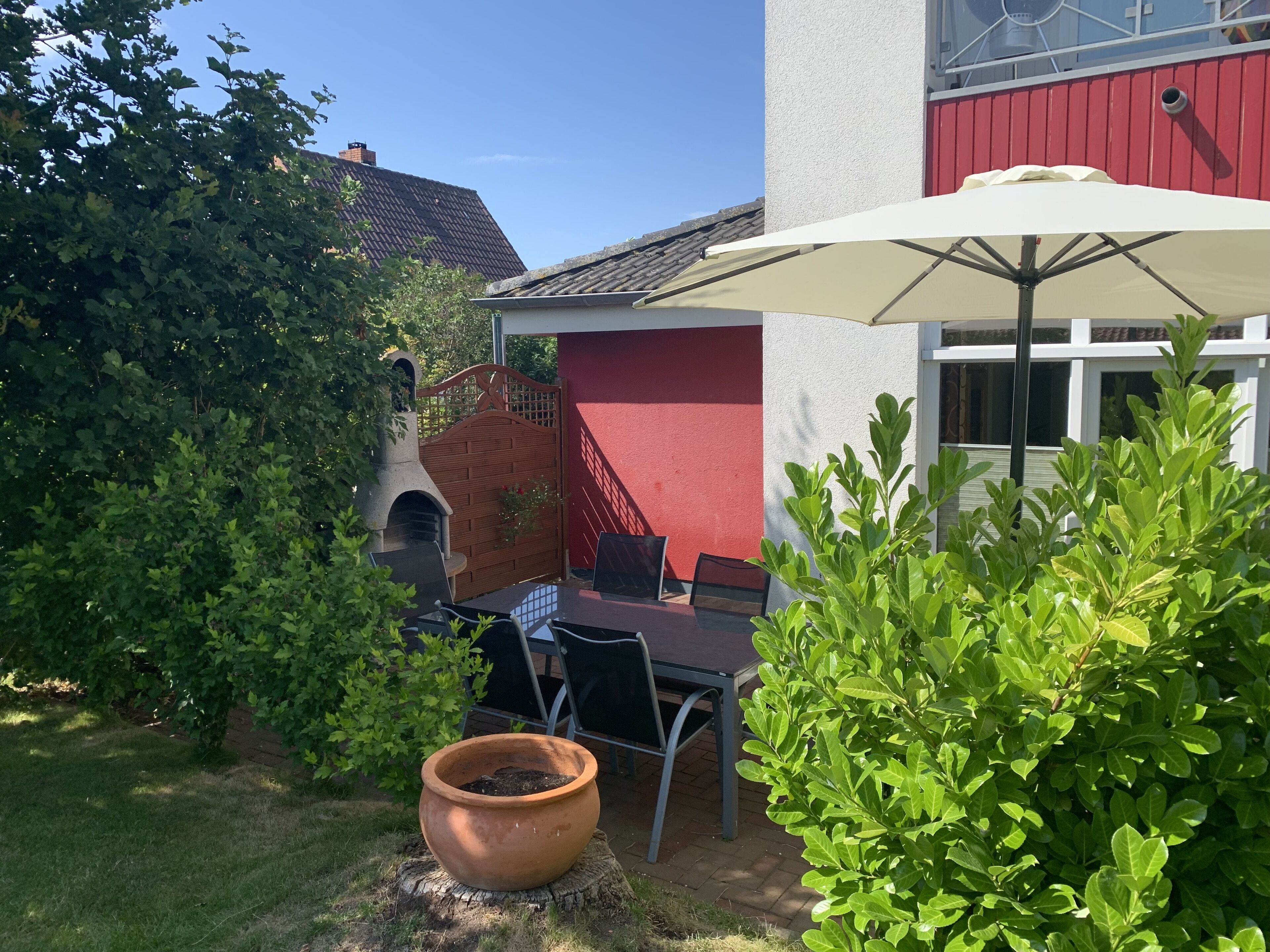 A patio with a table and chairs, a large potted plant, and a red building in the background.