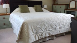 A neatly made bed with a white duvet and two green pillows in a room with a dark headboard, light green nightstands, and a framed picture on the wall.