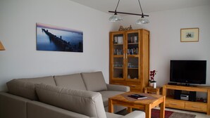 Een woonkamer met een bank, een houten kast, een televisie en een schilderij aan de muur.