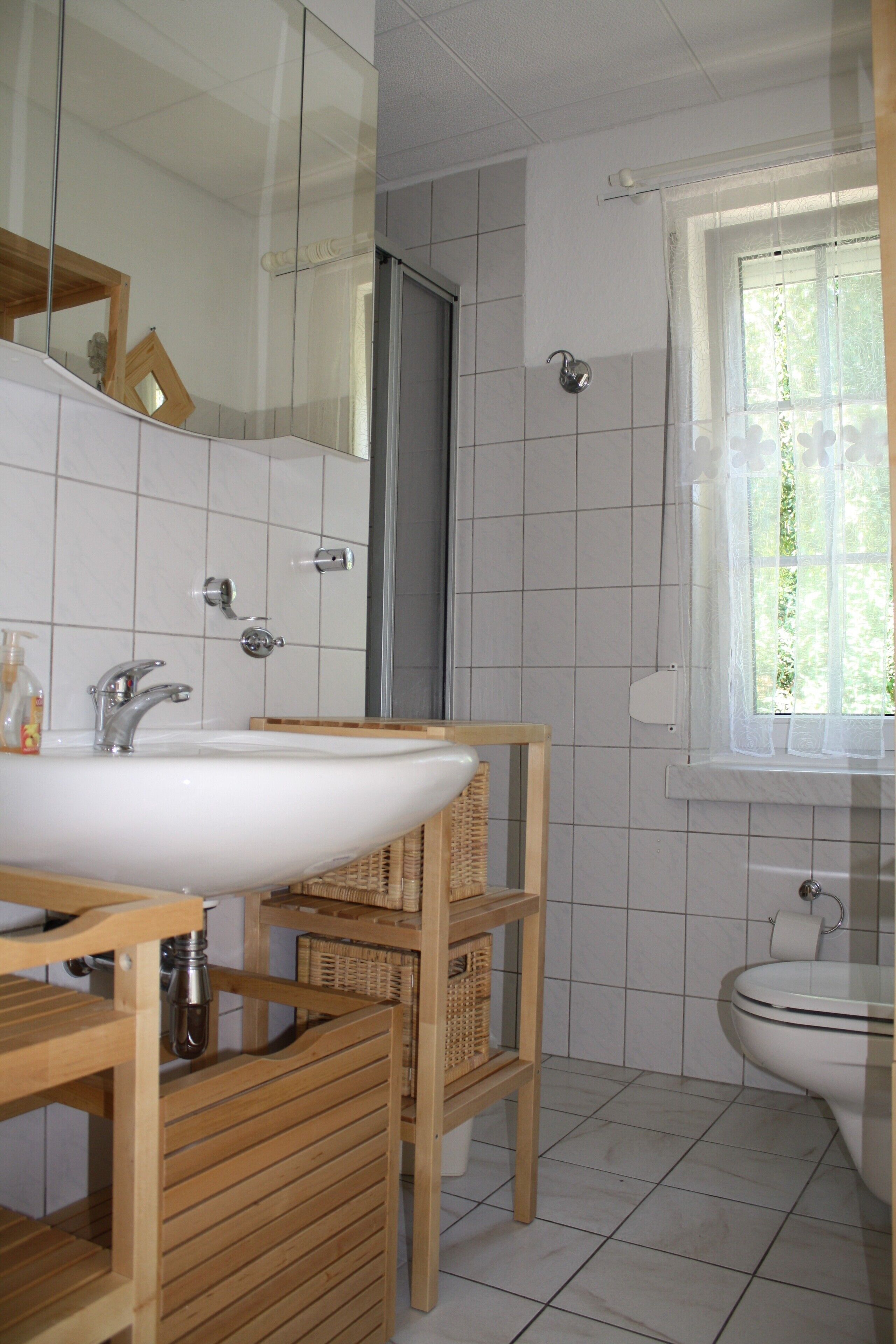 A bathroom with a white sink, wooden shelves, a mirror, and a window with a view of greenery.