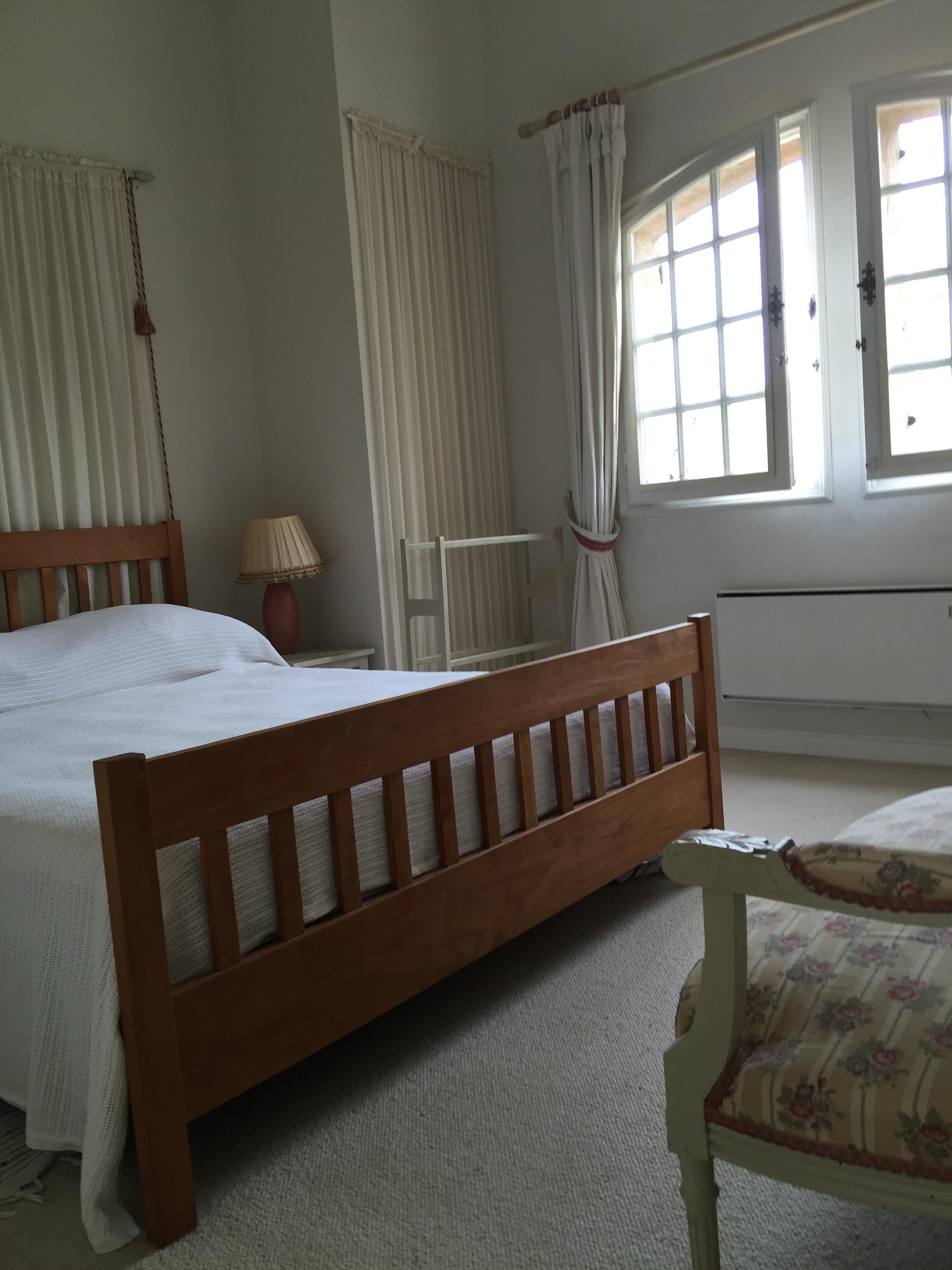 A bedroom with a wooden bed, a chair, a nightstand, and a window with curtains.