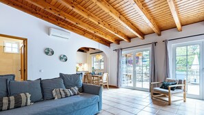 A living room with a blue sofa, a wooden coffee table, and a wooden chair. There is a kitchen visible through an open door. - Quinta da Liberdade: Spacious Cottage (4 persons) (Montinhos Da Luz)