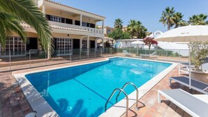 A swimming pool with a clear blue water, surrounded by a white fence, and a building with balconies and windows in the background. - Quinta da Liberdade: Spacious Cottage (4 persons) (Montinhos Da Luz)