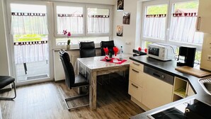 A modern kitchen with a wooden floor, a dining table with chairs, a microwave, a coffee maker, and a sink.