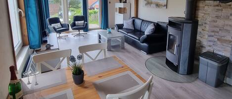 A cozy living room with a wooden ceiling, a fireplace, and a dining area with a table and chairs.