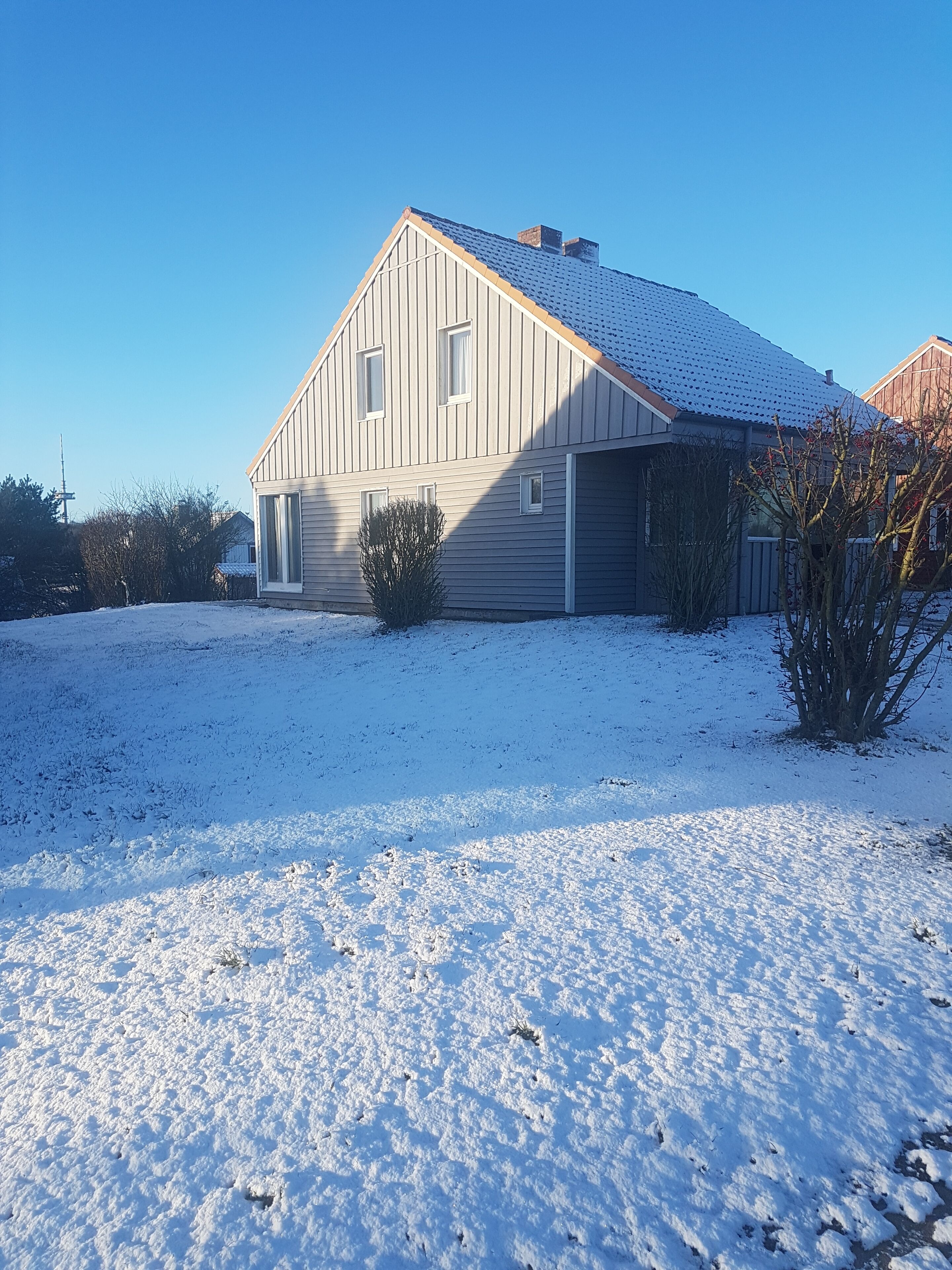 A two-story house with a sloped roof, a front porch, and a snow-covered yard.