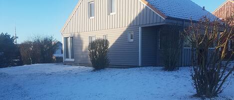 A two-story house with a sloped roof, a front porch, and a snow-covered yard.