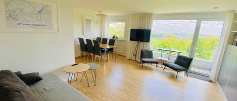 Een ruime woonkamer met een bank, een eettafel met stoelen, een televisie en een balkon met uitzicht.