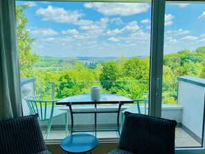 A balcony with a glass table and chairs, a vase, and a scenic view of a green landscape. - Perfect hotel alternative with style and charm at the edge of the Ruhr Area (Hattingen)