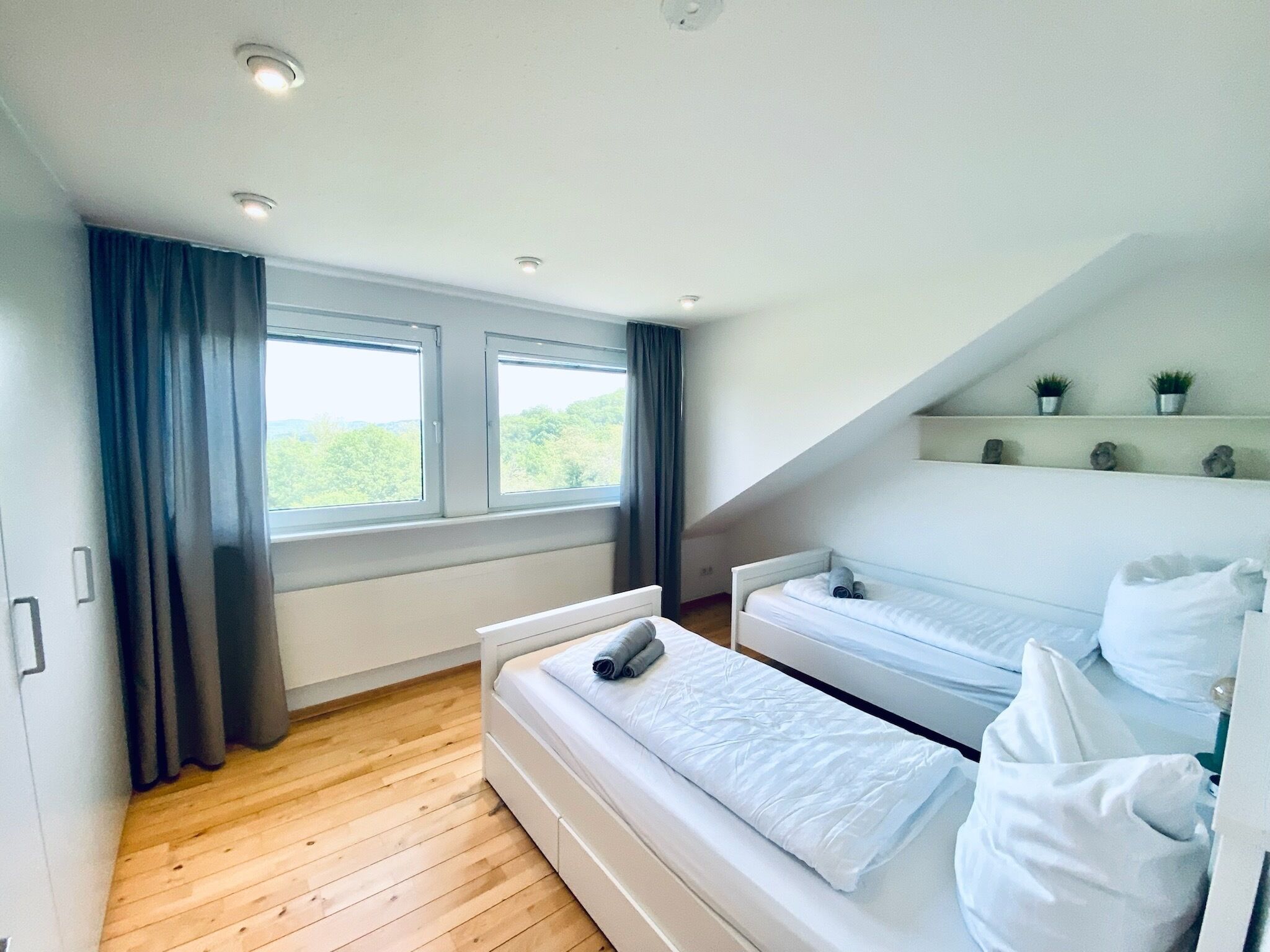 Une chambre avec deux lits, un plancher en bois, une fenêtre avec des rideaux et un plafond en pente.