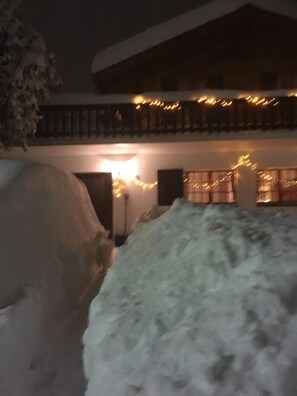 Un espacio exterior cubierto de nieve con un edificio, luces colgantes y un árbol nevado.