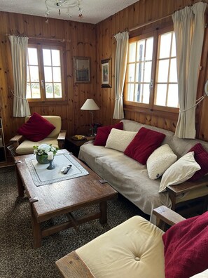 Habitación acogedora con paredes de madera, un sofá, una silla, una mesita de madera y una lámpara.