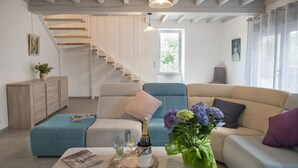 Ein modernes Wohnzimmer mit Treppe, einer Sofagarnitur, einem Couchtisch mit Flasche und Gläsern sowie einem Fenster mit Vorhängen.