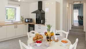 Eine moderne Küche mit weißen Schränken, einer schwarzen Dunstabzugshaube und einem Essbereich mit einem für das Frühstück gedecktem Tisch.