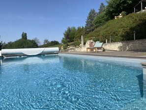 Una piscina cristalina con terraza de madera y sillas de descanso, rodeada de follaje y un muro de piedra.