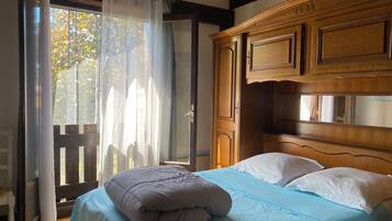 A bedroom with a bed, wooden headboard, and a view of trees through a window with sheer curtains.