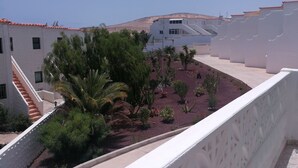 A courtyard with a white building, palm trees, and a red-tiled roof. - Beautiful apartment to feel good and relax (Costa Calma)