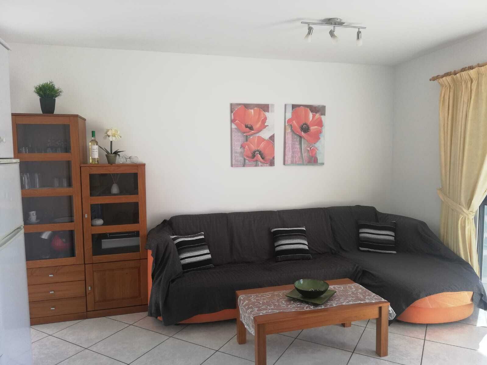 A living room with a dark sofa, a wooden cabinet, and two wall-mounted flower paintings.
