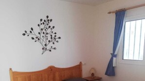A single bed with a wooden headboard, a wall decoration, a window with blue curtains, and a bedside table with a lamp. - Beautiful apartment to feel good and relax (Costa Calma)