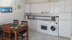 A compact kitchen with white cabinets, a built-in oven, a washing machine, and a dining area with a wooden table and chairs. - Beautiful apartment to feel good and relax (Costa Calma)