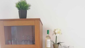 A wooden cabinet with multiple glass shelves, a potted plant, a bottle of wine, and a vase with flowers. - Beautiful apartment to feel good and relax (Costa Calma)