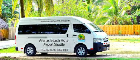 Una camioneta blanca con la leyenda "Arenas Beach Hotel Airport Shuttle" e información de contacto.