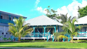 A two-story building with a white exterior and blue accents, featuring a covered porch and a staircase leading to the upper level. - Arenas Beach Hotel (Corn Islands)