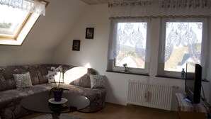 Un soggiorno con un divano, un tavolino rotondo, un'orchidea in vaso e una televisione su un mobile.