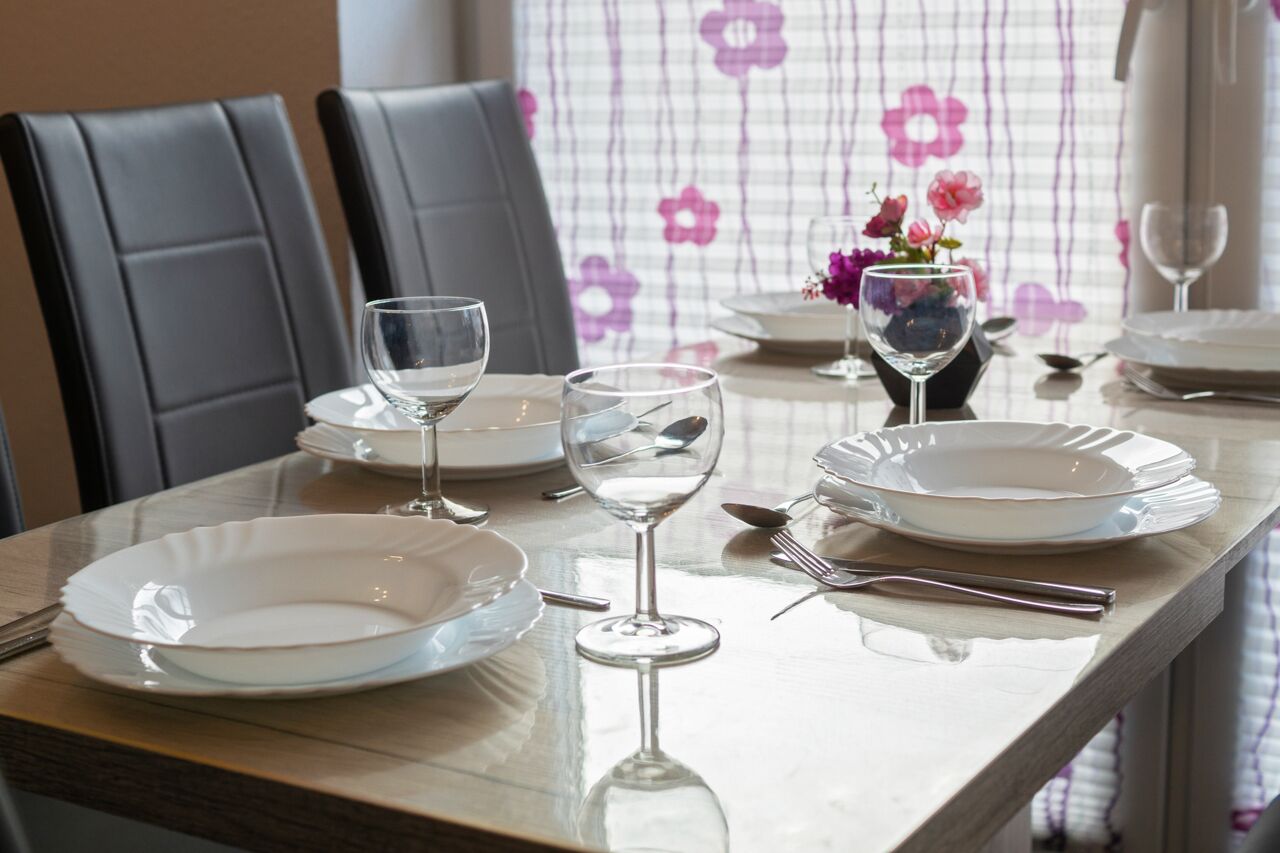 Una mesa de comedor dispuesta con platos, vasos y cubiertos, con un jarrón de flores al fondo.