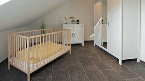 A room with a wooden crib, a white wardrobe, and a cabinet with decorative items. - Vacation home Lucky with pet (Norden)