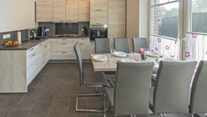 A modern kitchen with light wood cabinets, a dining area with a table set for four, and a large window with a view of the outside. - Vacation home Lucky with pet (Norden)