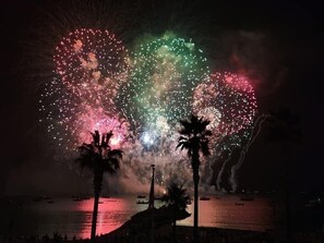 A nighttime beach scene with fireworks, palm trees, and boats on the water. - Magnificent air-conditioned apartment, sea view, elevator, Internet, Parking (Cavalaire-Sur-Mer)