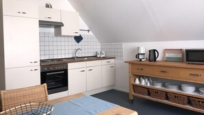 A modern kitchen with white cabinets, a built-in oven, a coffee maker, and a television on a wooden shelf. - new in 2019 !! Our apartment has been lovingly furnished for you (Minderlittgen)