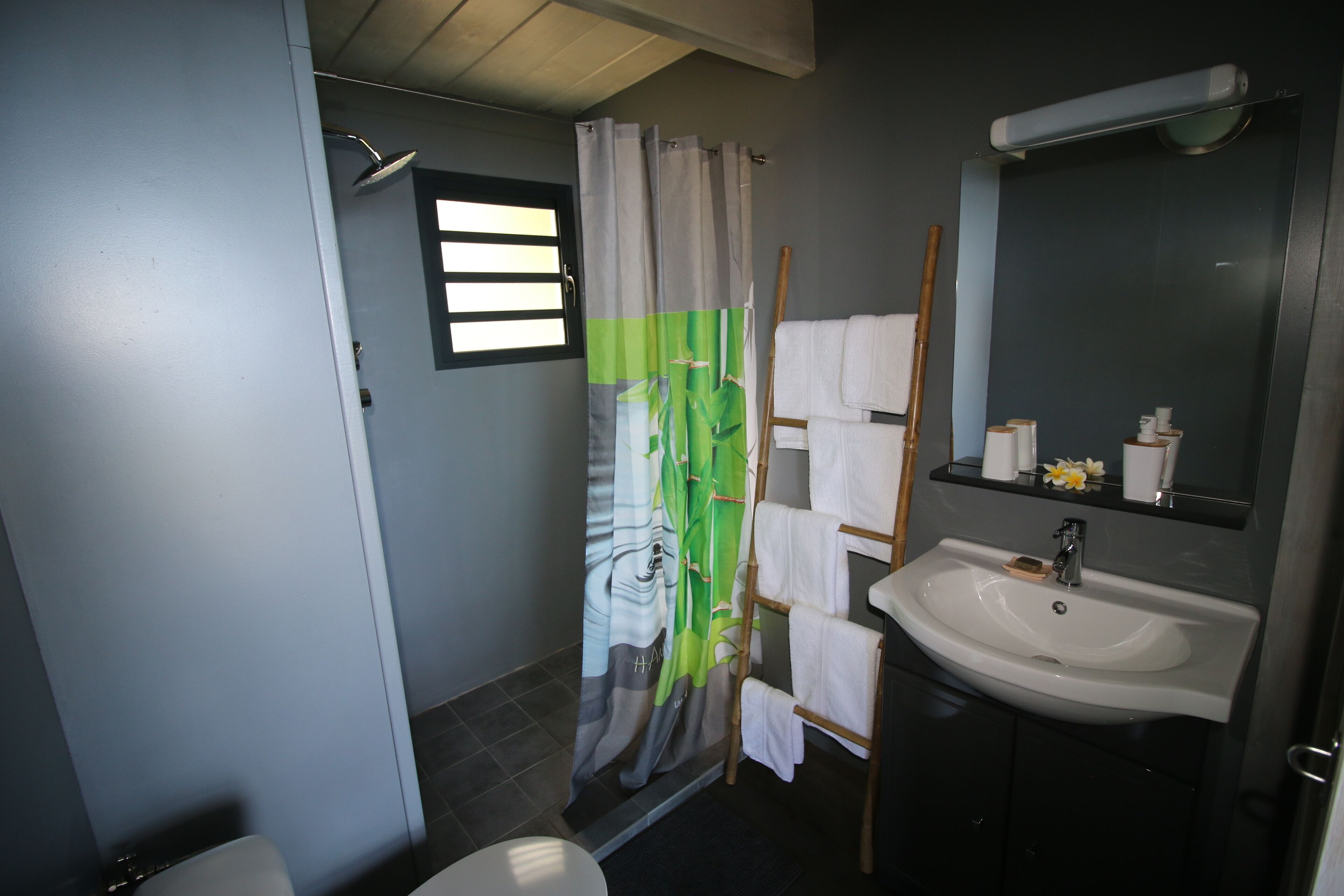 A bathroom with a shower curtain, a sink, a mirror, and a towel rack.