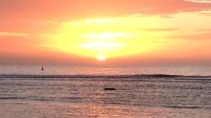 Un coucher de soleil sur l’océan, avec un bateau à l’horizon.