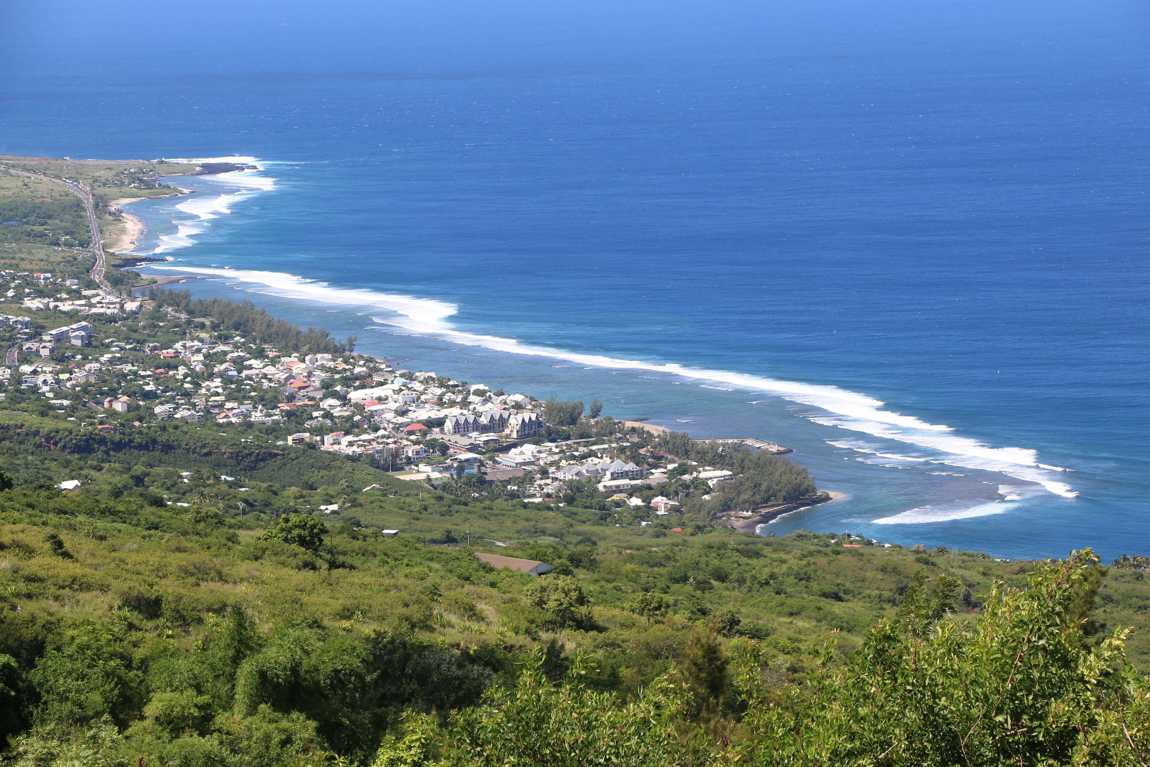 A coastal town with a mix of residential and commercial buildings, a clear view of the ocean, and a hilly landscape.