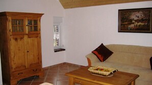 A living room with a wooden cabinet, a sofa, a coffee table with a basket, and a painting on the wall. - Lone-standing vacation home with a large garden in a peaceful location (Niedersachsen)
