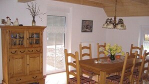 A dining area with a wooden table and chairs, a cabinet with glass doors, and a hanging light fixture. - Lone-standing vacation home with a large garden in a peaceful location (Niedersachsen)