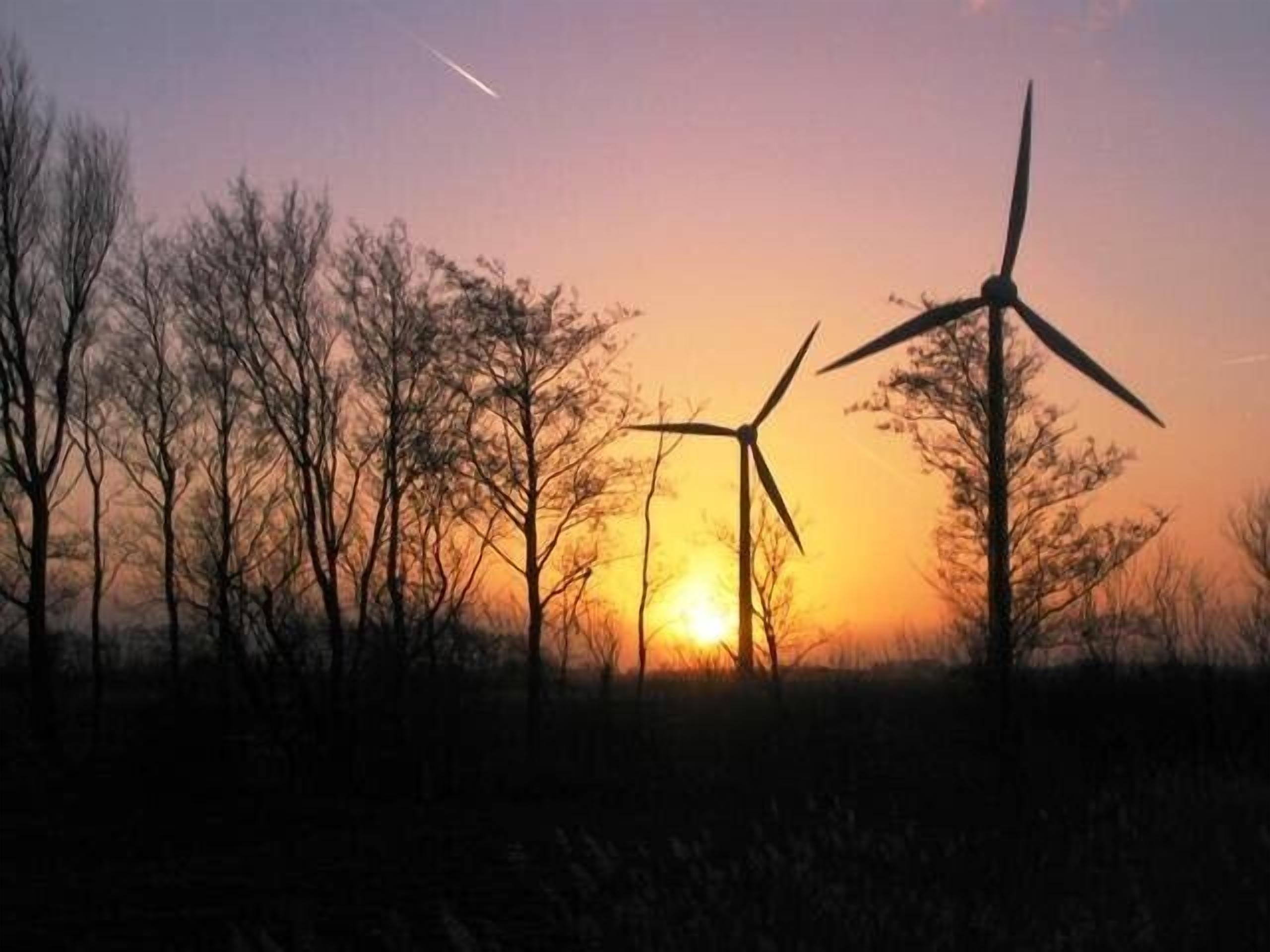 A landscape with wind turbines silhouetted against a sunset.